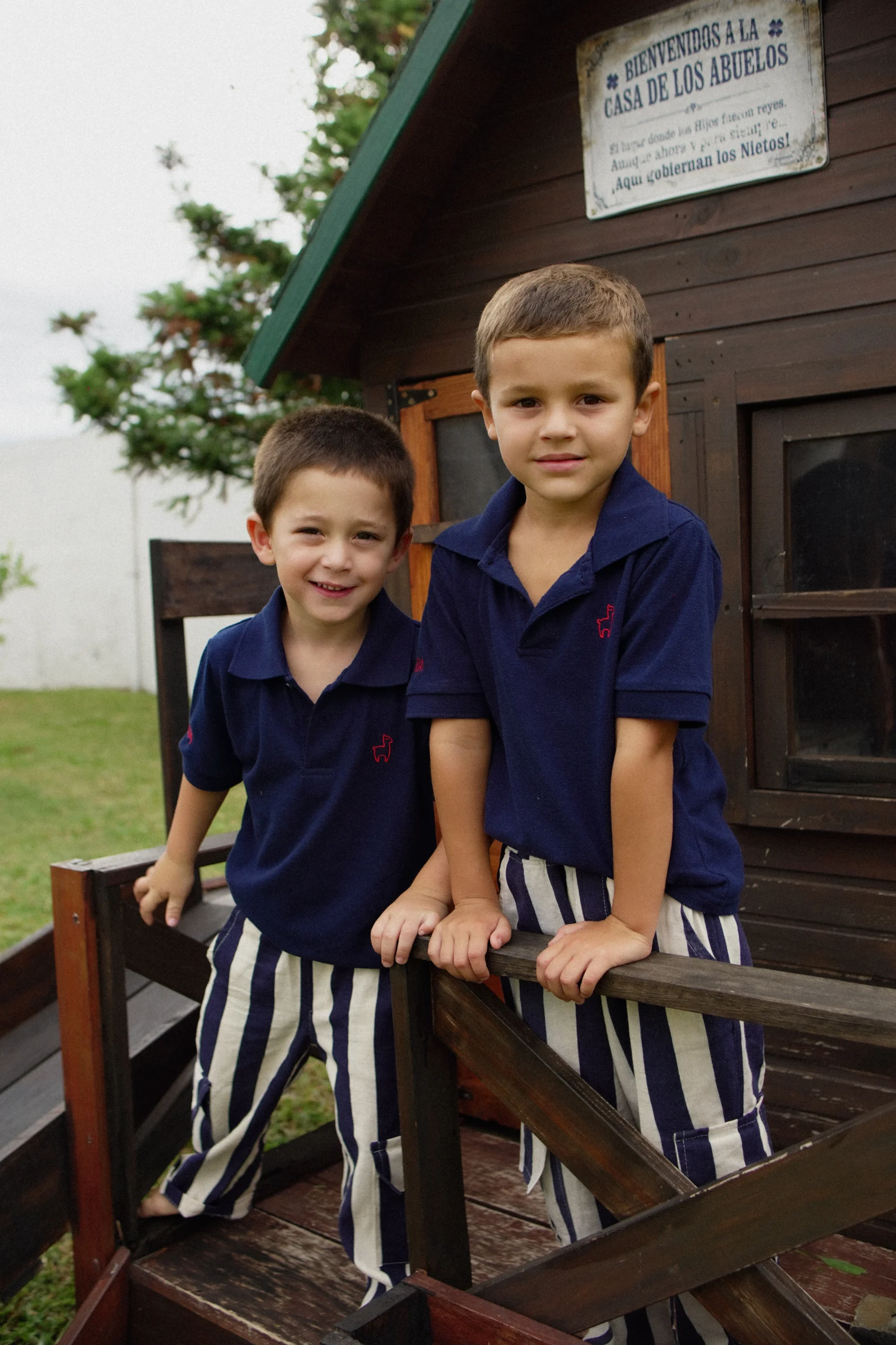 Dos niños sentados en escalones de casita con polos azul marino Infantem