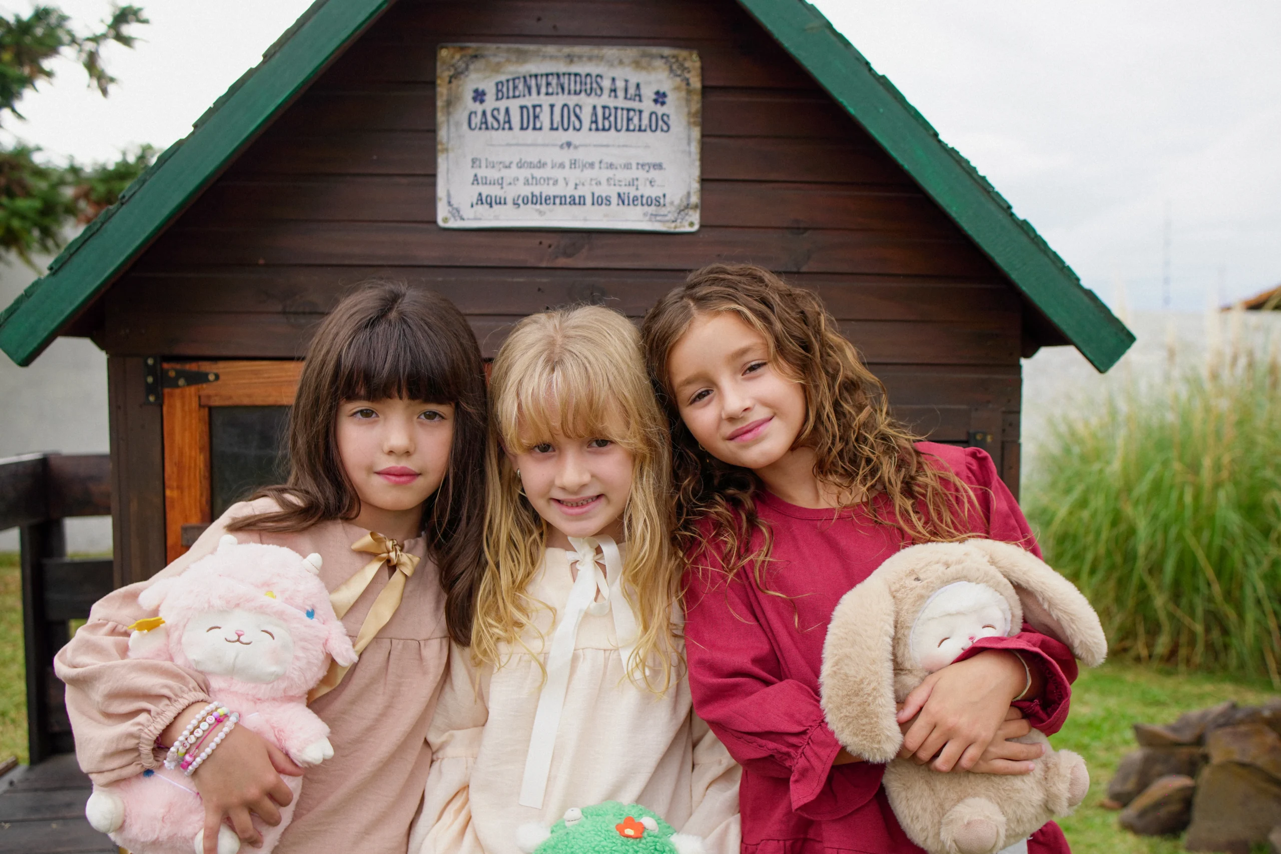 Tres niñas abrazadas con peluches frente a casita de madera Infantem