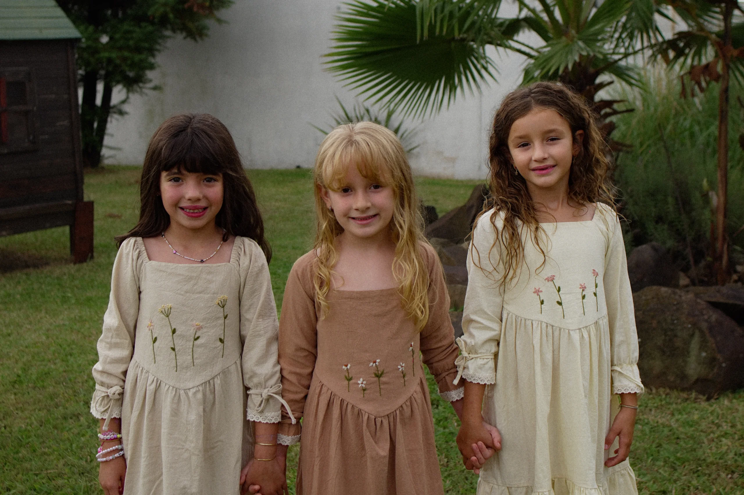 Tres niñas con vestidos en tonos naturales y detalles florales Infantem